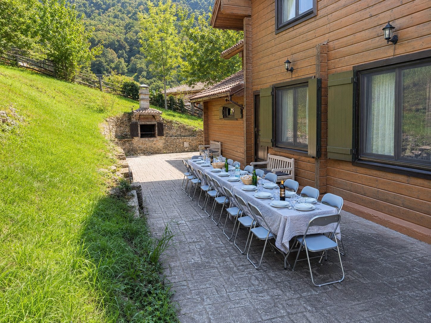 Mesa larga puesta en la terraza exterior, con la barbacoa de piedra al fondo